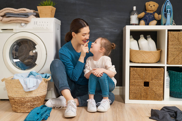 Beautiful young woman and child girl little helper are having fun and smiling while doing laundry at home.                                - 写真・画像