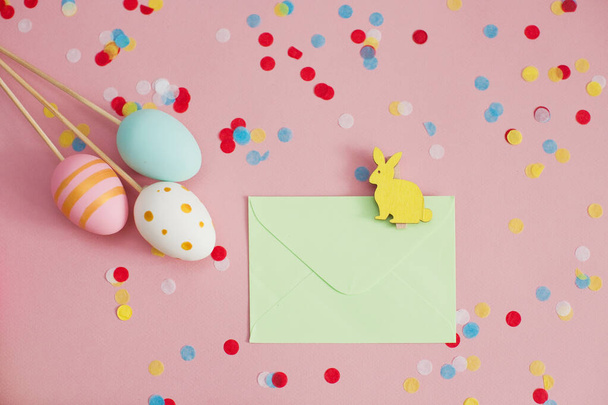 Easter eggs and envelope with easter bunny on a pink background with colorful confetti. Easter decorations - Photo, Image