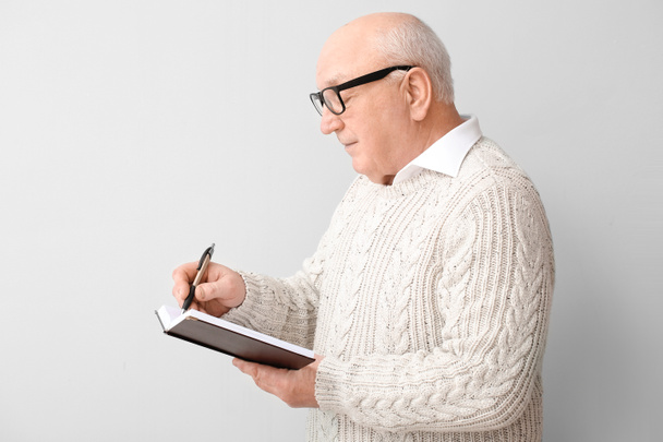 Portrait of elderly man with notebook on light background - Foto, Imagem