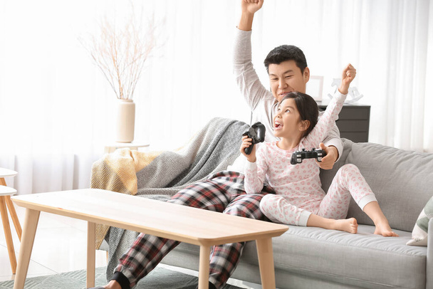 Aziatisch man en zijn kleine dochter spelen video game thuis - Foto, afbeelding