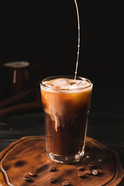 Pouring of milk into cold coffee in glass on table - Foto, afbeelding