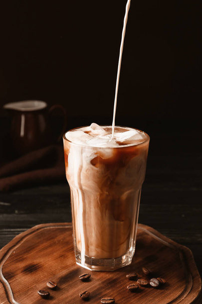 Pouring of milk into cold coffee in glass on table - Photo, Image