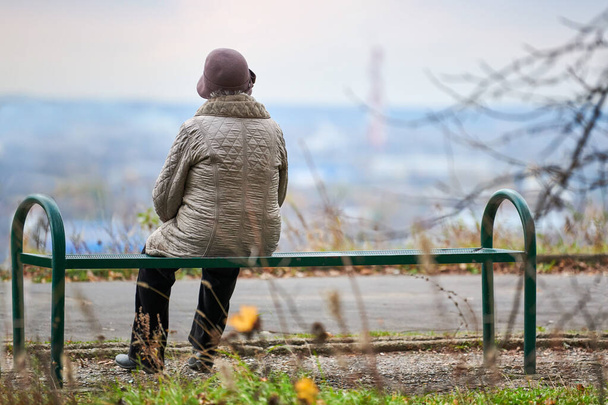 Staruszka siedzi na ławce w jesiennym parku miejskim. Samotna wdowa patrząca głęboko w miasto, z autorefleksją. Babcia marzy o swojej koncepcji rodzinnej. - Zdjęcie, obraz