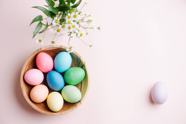 Imagen de Pascua, huevos multicolores en un plato de madera, sobre un fondo rosa. Hay un lugar para su texto
 - Foto, Imagen