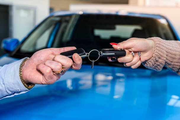 Männliche Hand mit Autoschlüssel gegen Neuwagen im Verkaufsraum - Foto, Bild
