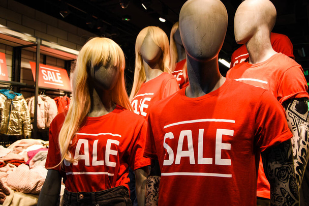 διακόσμηση της εισόδου του καταστήματος στο εμπορικό κέντρο. πινακίδα πώληση με λευκά γράμματα σε κόκκινο φόντο.εκπτώσεις στο εμπορικό κέντρο, Mannequins σε ένα παράθυρο ενός καταστήματος ρούχων σε T-Shirts με πινακίδες Διαφήμιση Πώληση - Φωτογραφία, εικόνα
