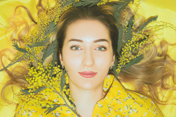 Portrait of young pretty woman with mimosa on the yellow background closeup. - Foto, afbeelding