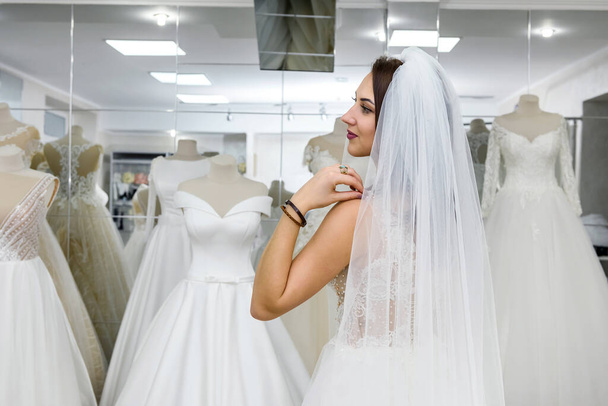 Приваблива молода жінка в весільній сукні в магазині нареченої
 - Фото, зображення