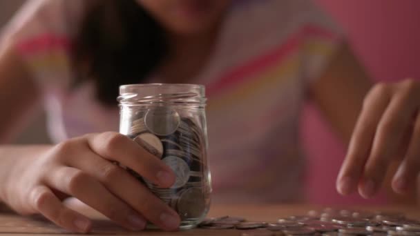 Een klein meisje stopt geld in een glazen pot voor toekomstige kosten. Begrip "spaargeld". - Video