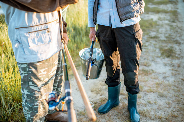 Holding fishing rods and bucket with fish outdoors - Foto, afbeelding