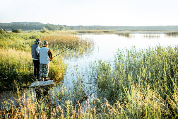 Дедушка со взрослым сыном рыбачит на озере
 - Фото, изображение