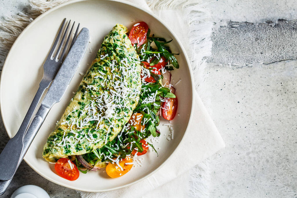 Green spinach omelet with cheese, arugula and tomatoes on a white plate, copy space. - Photo, Image