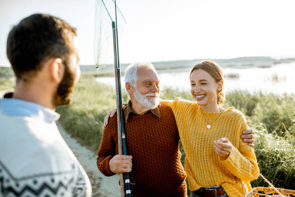 Young man and woman with senior grandfather having a good time while fishing - Foto, Imagen