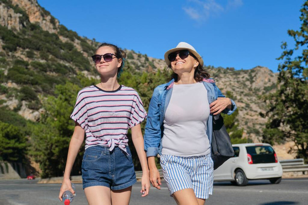 Two women mother and daughter teenager walking on sunny summer day on mountain road. Tourism, excursions, travel, family vacations - Fotografie, Obrázek