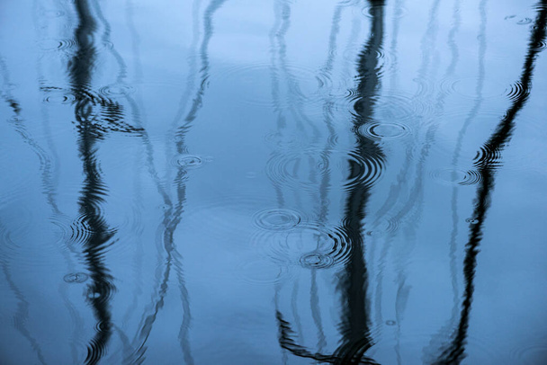 Eine abstrakte Nahaufnahme der Oberfläche eines Sees in England, mit interessanten Spiegelungen und Regentropfen, die auf das Wasser treffen. - Foto, Bild