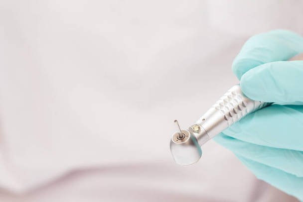 Close-up dentist's hand in a latex examination glove with high-speed dental handpiece on blurred background. Medical tools concept. Shallow depth of fiel. - Photo, Image
