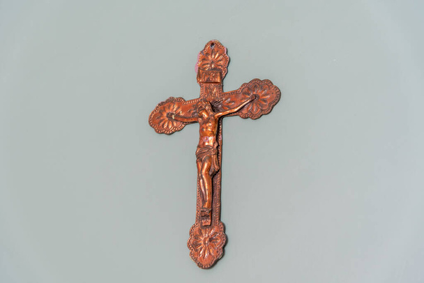 Image of an old crucifix hanging on the masonry wall made of galvanized iron and artificially aged. Religious artifact. Symbol of the Catholic Church and the Crucifixion of Christ. - Фото, изображение