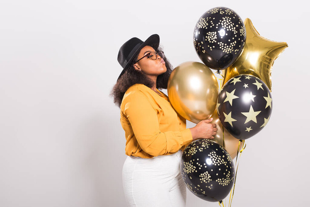 Holidays, party and fun concept - Portrait of smiling young African-American young woman looking stylish on white background holding balloons. - Fotoğraf, Görsel