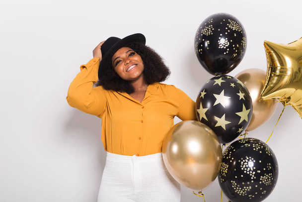 Vacanze, festa e divertimento - Ritratto di giovane donna afro-americana sorridente in cerca di stile su sfondo bianco con palloncini
. - Foto, immagini
