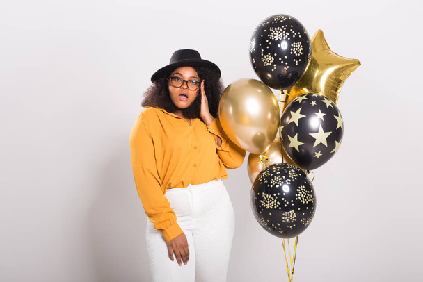 Holidays, party en fun concept - Portret van lachende jonge Afro-Amerikaanse jonge vrouw op een stijlvolle witte achtergrond met ballonnen. - Foto, afbeelding