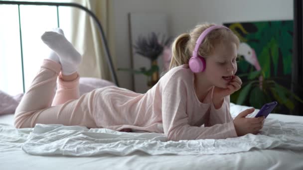 vida moderna de la generación Z. adolescente en pijama y auriculares en la habitación en la cama escucha música desde un teléfono inteligente
. - Metraje, vídeo