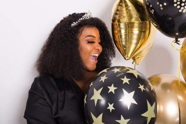 Holidays, puolue ja hauska konsepti - Muotokuva hymyilevä nuori Afrikkalainen Amerikan nuori nainen näyttää tyylikäs valkoisella taustalla tilalla ilmapalloja
. - Valokuva, kuva