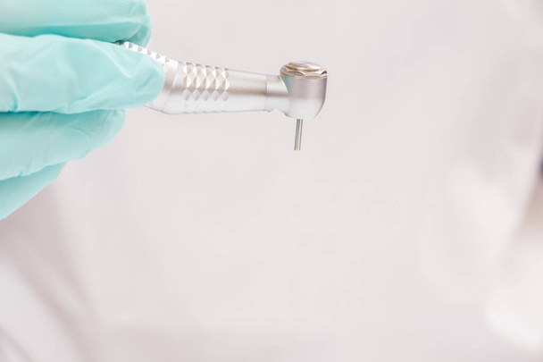 Close-up tandarts 's hand in een latex handschoen met hoge snelheid tandheelkundige handstuk op wazige achtergrond. Medisch gereedschap concept. Ondiepe diepte van fiel. - Foto, afbeelding