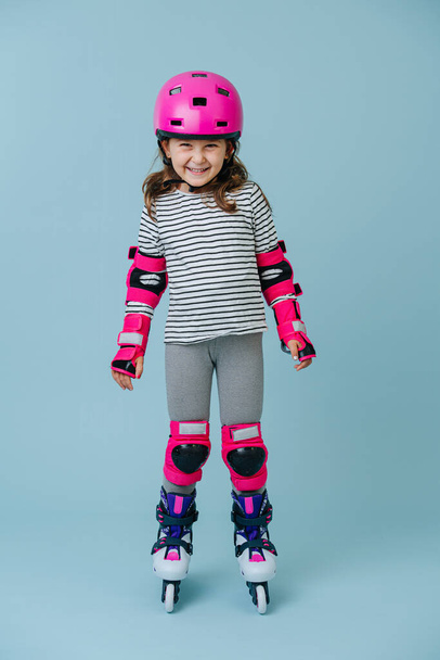 Full-length roller skating girl in protective gear on the blue background - 写真・画像
