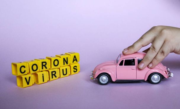 розовый автомобиль в руках ребенка разбивает надпись коронавирус из пластиковых букв. Концепция восстановления от коронавируса и победы над вирусом
. - Фото, изображение