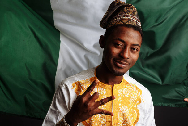 Homme africain avec des vêtements traditionnels pose devant la caméra, souriant et s'amuse devant le drapeau du Nigeria
 - Photo, image
