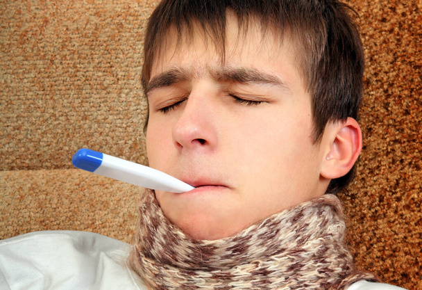 Tired Young Man with a Medical Thermometer on the Sofa at the Home - Foto, Imagem
