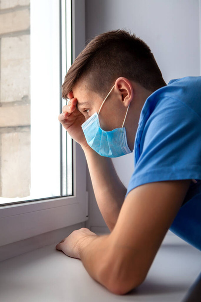 Young Man in a Flu Mask by the Window in the Room - Photo, image