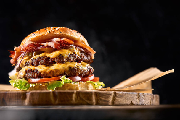 Saftiger Burger auf dem Brett, schwarzer Hintergrund. Dunkler Hintergrund, Fast Food. Traditionelles amerikanisches Essen. Kopierraum. - Foto, Bild