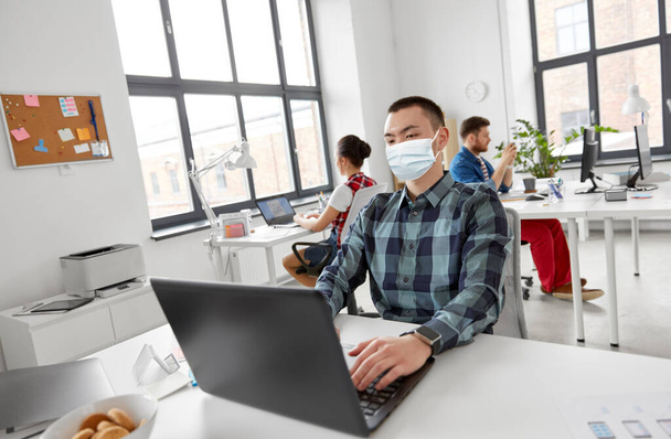 man in medical mask with laptop working at office - Zdjęcie, obraz