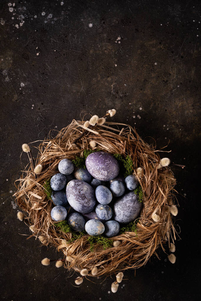 Colorful easter eggs in a nest on a dark background. Easter card. Top view. Copy space.  - Photo, Image