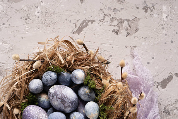Colorful easter eggs in a nest with a light purple cheesecloth on a gray background. Easter card. Top view. Copy space.  - Фото, изображение