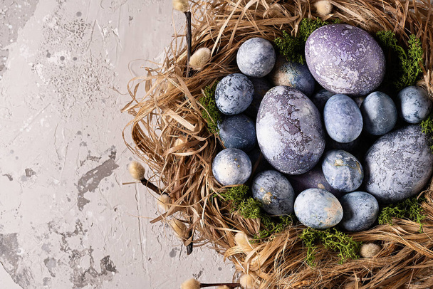 Colorful easter eggs in a nest on a gray background. Easter card. Top view. Copy space.  - Photo, Image
