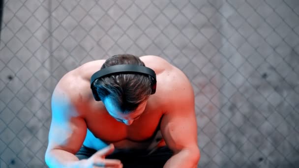 Atrakcyjny bokser w słuchawkach siedzący na ławce - Materiał filmowy, wideo