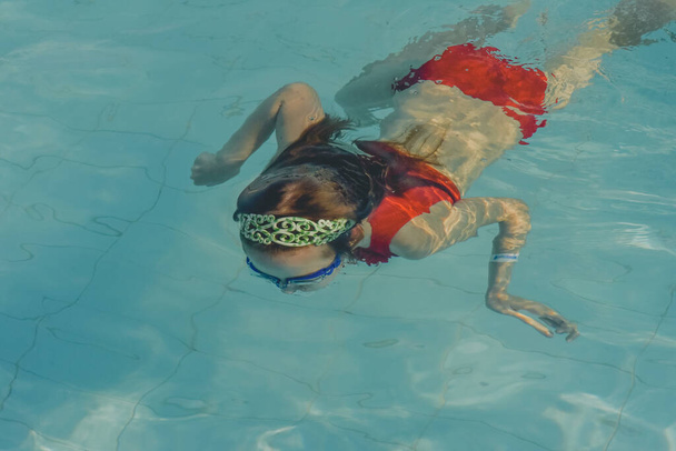 Cute girl with goggles in swimming pool. Girl swims in the pool with goggles. Summer, pool, relaxation, water park, relaxation area. The baby is swimming. Hello summer. Hooray, holidays. health - Photo, Image