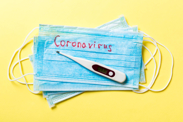 Top view of protective medical masks and a thermometer on yellow background. Coronavirus word. Ncov and covid epidemic. Pandemic concept. Protect your health. - Zdjęcie, obraz