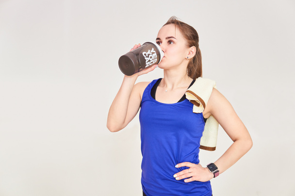 sierlijke atletische vrouw met een handdoek drinkt uit een shaker fles voor sportdrank na de training - Foto, afbeelding