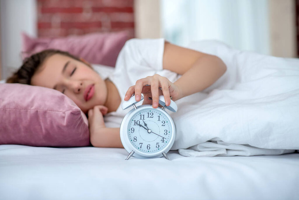 Sleeping teenager girl in bed, hand on the alarm clock. - Photo, image