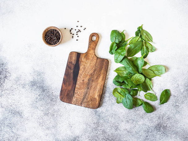 Wooden cutting board mock up, spices in a wooden bowl and fresh spinach on a gray background. Top view. Copy space - Фото, изображение
