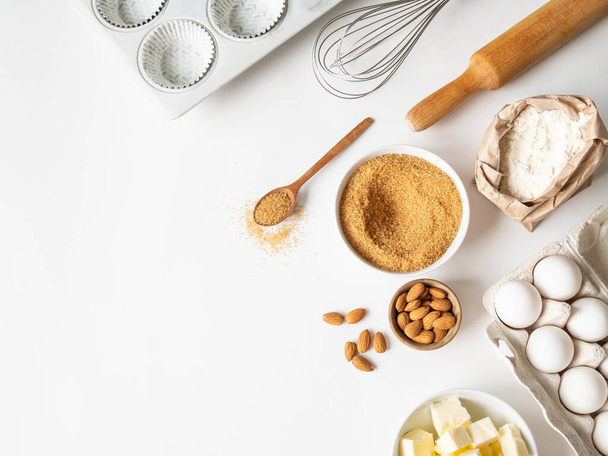 Set of various baking ingredients - flour, eggs, sugar, butter, nuts, kitchen utensils and cupcake baking dish on white background. Top view. Copy space - 写真・画像
