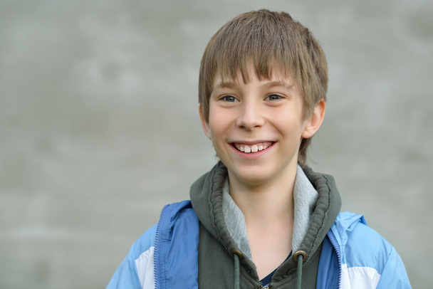 Portrait of attractive happy smiling 11 years old boy, outdoor over gray wall. Happy handsome teenager. Cute kid's portrait. - Fotoğraf, Görsel