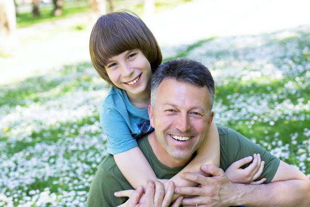 Πορτρέτο του πατέρα με το γιο του στο πάρκο καλοκαίρι διασκέδαση. Piggyback. Οικογενειακή διασκέδαση. Ευτυχισμένο αγόρι που παίζει με τον μπαμπά καλοκαίρι φύση εξωτερική - Φωτογραφία, εικόνα