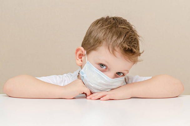 Cute boy of four years in a medical mask. Quarantined children due to an epidemic. The boy sits at home sad and lonely - Photo, Image