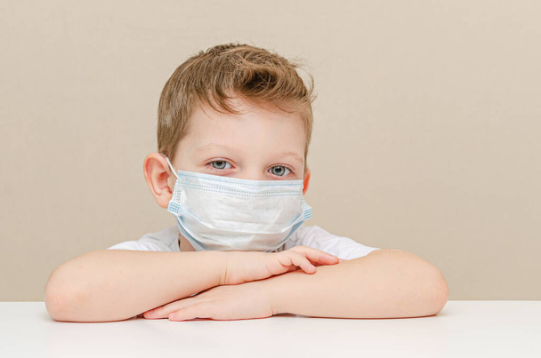 Χαριτωμένο αγόρι τεσσάρων ετών με ιατρική μάσκα. Παιδιά σε καραντίνα λόγω επιδημίας. Το αγόρι κάθεται στο σπίτι λυπημένο και μοναχικό - Φωτογραφία, εικόνα