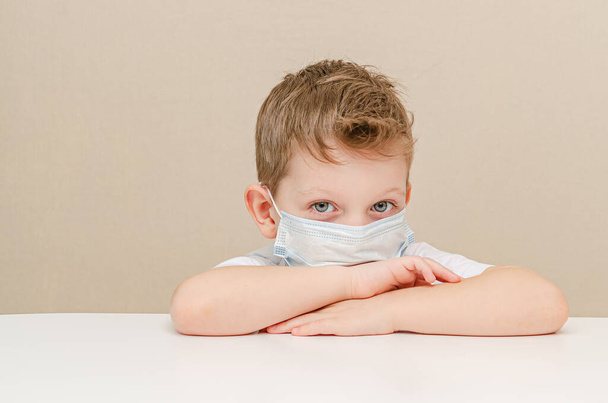 Roztomilý čtyřletý chlapec v lékařské masce. Děti v karanténě kvůli epidemii. Chlapec sedí doma smutný a osamělý - Fotografie, Obrázek