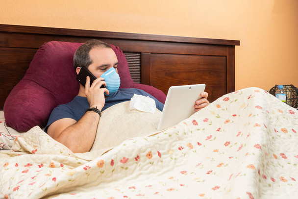 άρρωστος άνθρωπος χρησιμοποιώντας tablet και τηλέφωνο στο κρεβάτι. Τηλεεργασία - Φωτογραφία, εικόνα